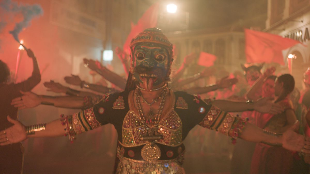 Lors d'une fête de rue, des personnages portant des masques et des vêtements traditionnels lèvent les bras selon un motif rappelant la déesse hindoue Shiva dans Monkey Man.