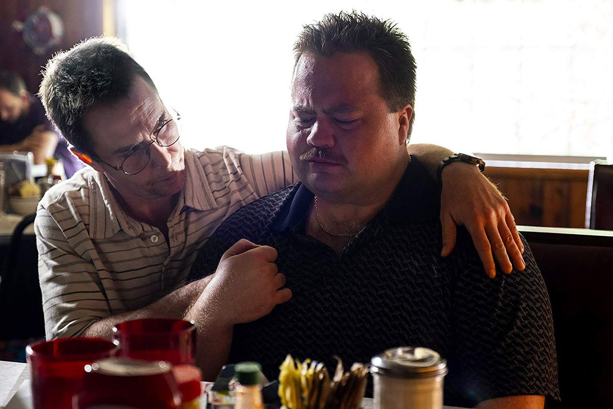 Un homme portant des lunettes consolant un homme désemparé assis à une table de restaurant.
