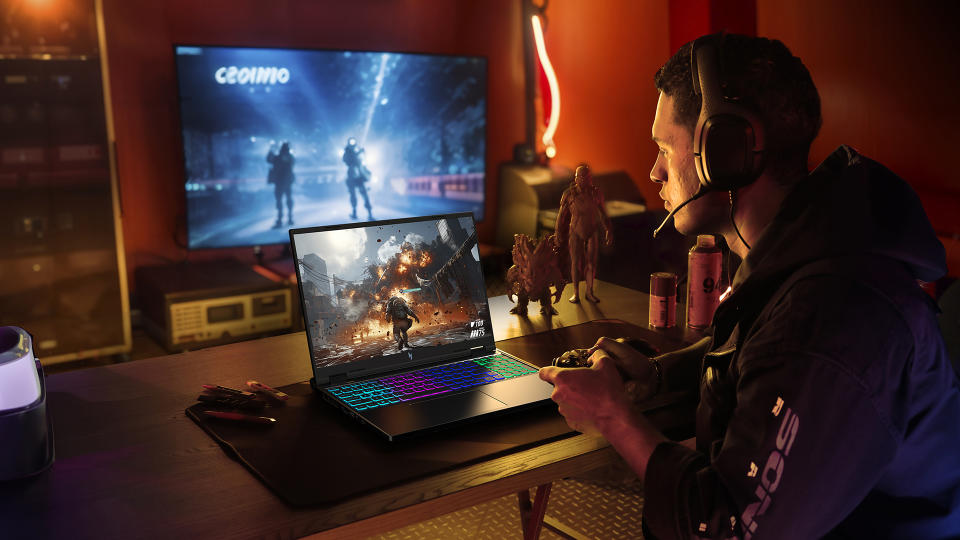 Un joueur est assis dans une salle de jeu chic et moderne avec un ordinateur portable de jeu Acer.  Un deuxième téléviseur montre une autre partie d'un jeu derrière eux.