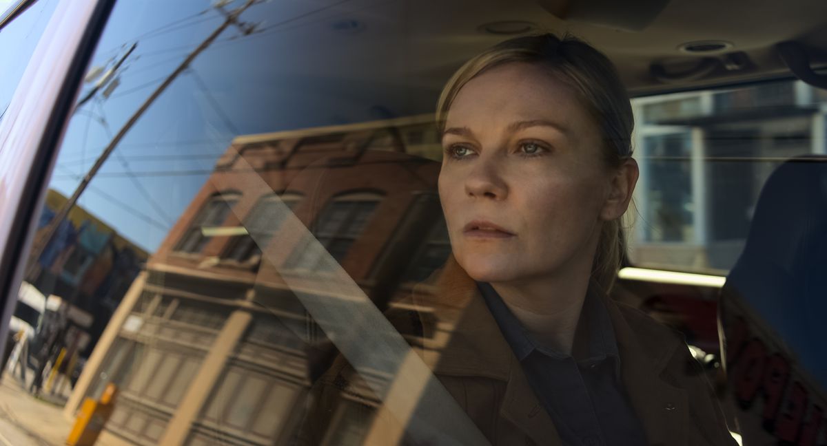 Le photojournaliste Lee Miller (Kirsten Dunst) est assis dans une voiture et regarde pensivement par la fenêtre la petite ville reflétée dans la vitre dans la guerre civile d'Alex Garland.