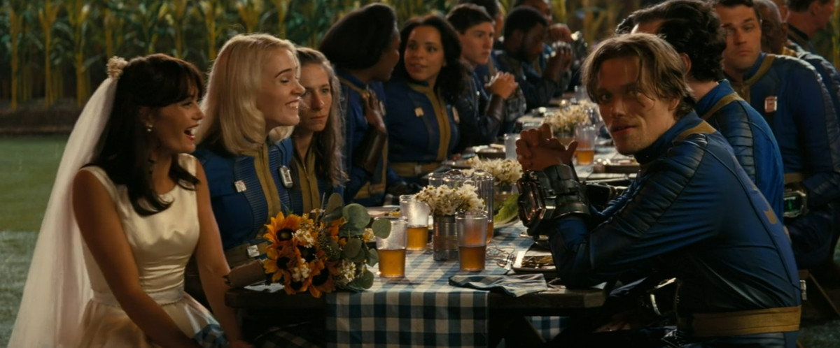 Ella Purnell, vêtue d'une robe de mariée, rit pendant que le reste de la noce parle à une table dans Fallout