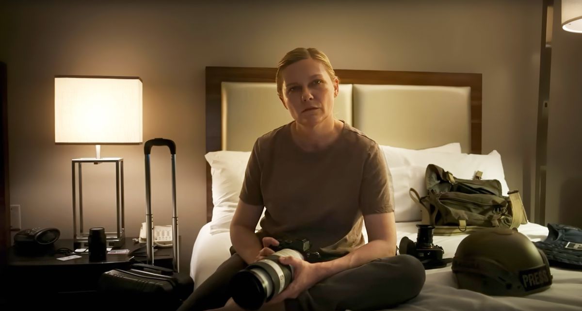 Le photojournaliste Lee (Kirsten Dunst) est assis sur le lit d'une chambre d'hôtel et regarde directement la caméra dans Civil War d'Alex Garland.