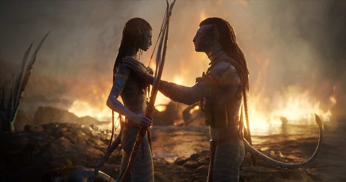 Jake Sully et Neytiri se réconfortent après la bataille, avec un feu rugissant derrière eux au-dessus de l'eau dans Avatar : La Voie de l'Eau.