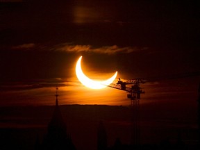 Une éclipse solaire annulaire s'élève au-dessus des grues de construction et de la Tour de la Paix sur la Colline du Parlement à Ottawa le jeudi 10 juin 2021.