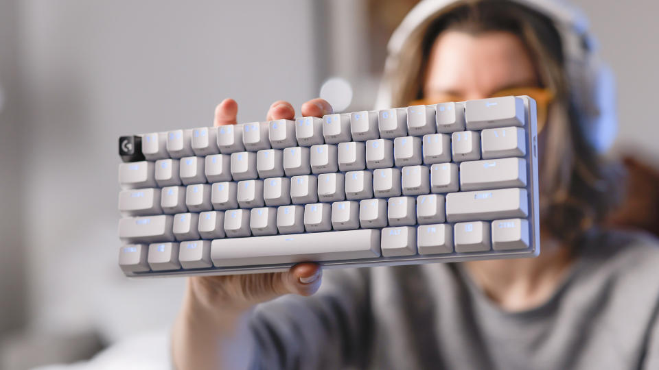 Une femme vêtue d'un pull gris tient un clavier de jeu Logitech G Pro X 60 blanc devant la caméra avec sa main gauche.