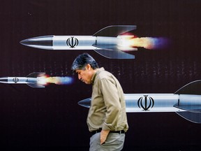 Ce mois-ci, un homme passe devant une banderole représentant des missiles dans une rue de Téhéran.  Pour la première fois dans l’histoire, Israël et l’Iran s’attaquent directement.