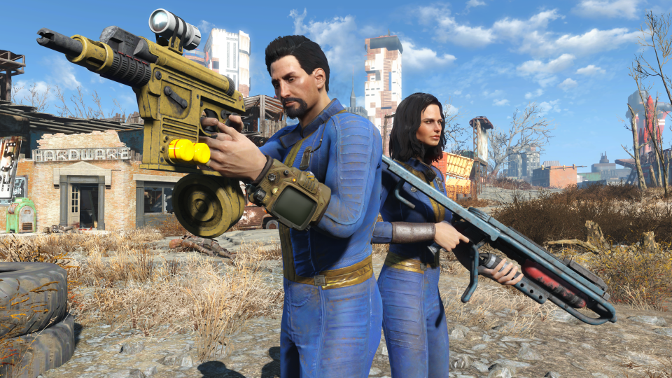 Capture d'écran promotionnelle pour la mise à jour de la console nouvelle génération pour Fallout 4. Deux personnes (portant un costume bleu) se tiennent armées d'armes à feu dans un désert de jeux vidéo.  Des bâtiments en ruine et un paysage désertique en arrière-plan.