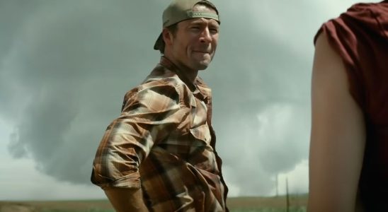 Glen Powell in the trailer for Twisters with a tornado behind him.