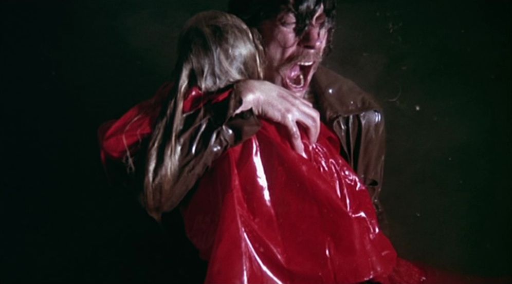 Un homme hurlant de douleur tout en tenant le corps d'une jeune fille vêtue d'un imperméable rouge trempé dans l'eau dans Don't Look Now.