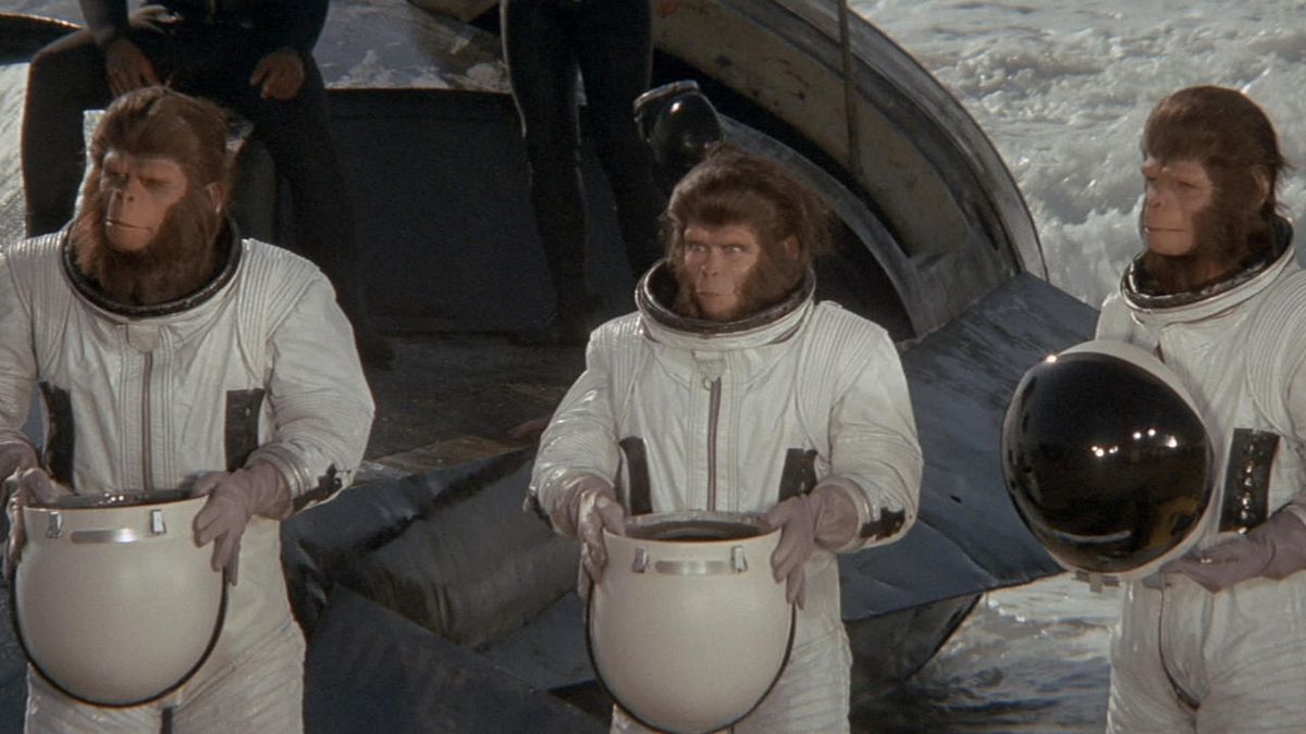 Trois singes en costume d'astronaute debout côte à côte tenant des casques dans Escape from the Planet of the Apes.