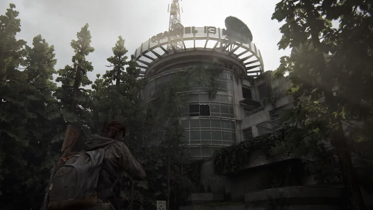 Ellie debout à l'extérieur et regardant à travers les arbres du bâtiment Channel 13 dans The Last of Us 2