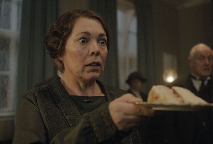 Olivia Colman, surprise, tient une part de gâteau sur une assiette dans Wicked Little Letters