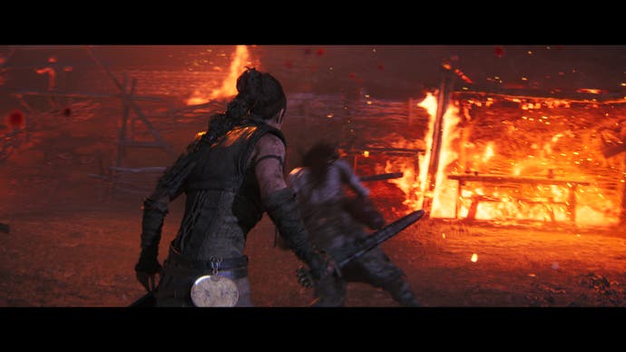 Capture d'écran de Hellblade 2 montrant Senua brandissant une épée devant un ennemi tandis qu'une maison brûle en arrière-plan