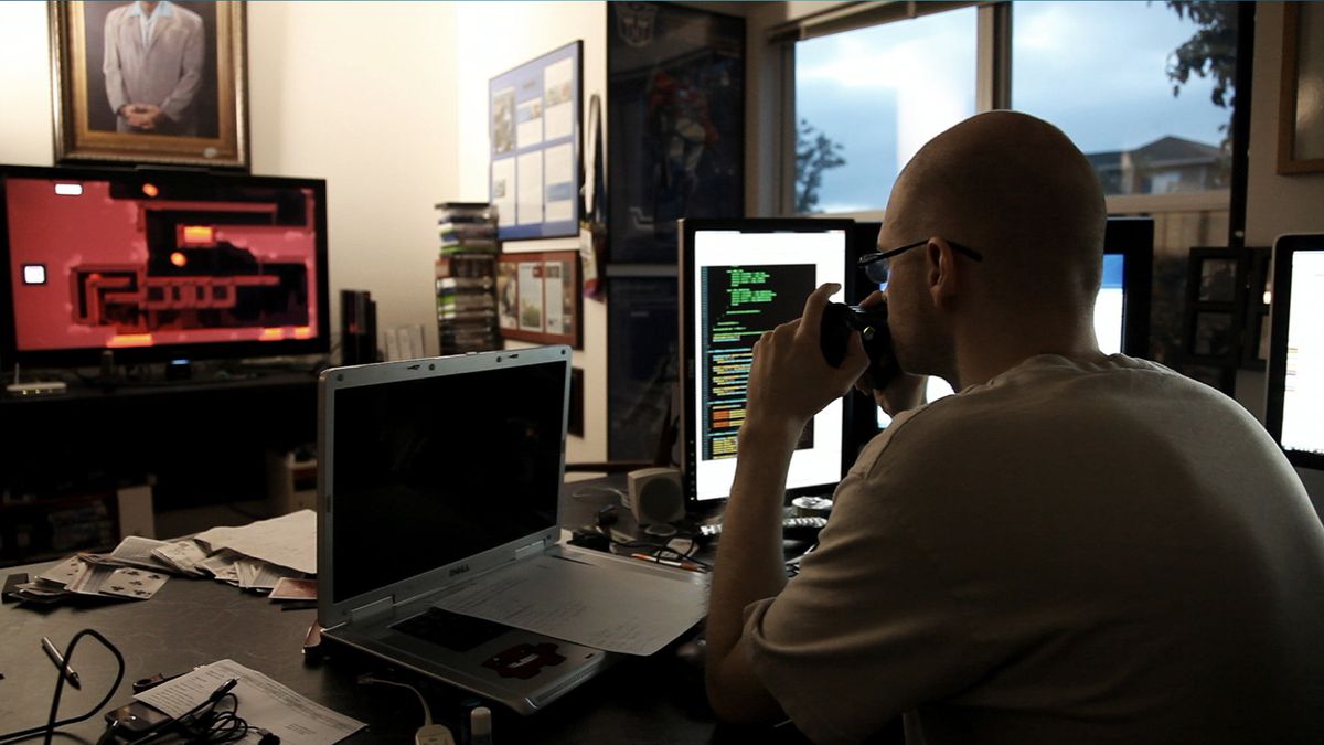 Tommy Refenes est assis à son bureau entouré d'écrans d'ordinateur, jouant à Super Meat Boy sur un téléviseur en arrière-plan