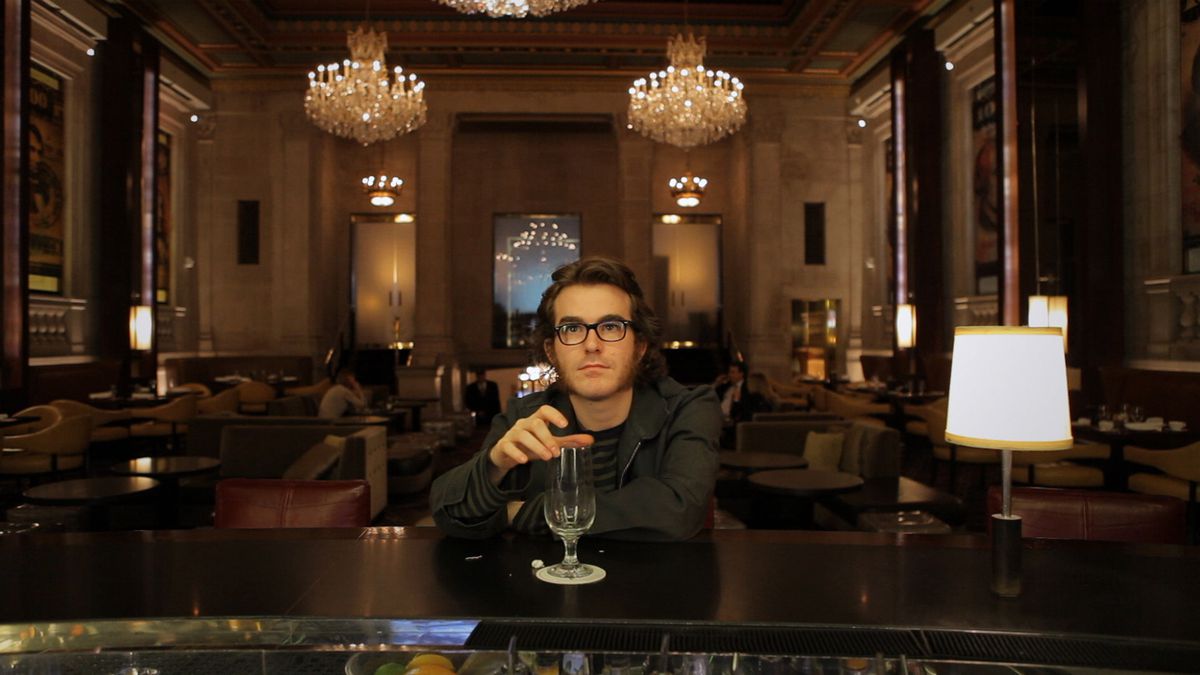Phil Fish, avec des lunettes hipster et des côtelettes de mouton, prend un verre dans un bar chic d'hôtel