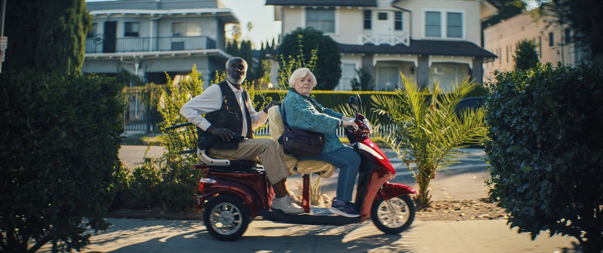June Squibb et Richard Round Tree dans le rôle de Thelma et Ben, regardent à leur droite alors qu'ils roulent sur le trottoir sur un scooter de mobilité biplace à Thelma.