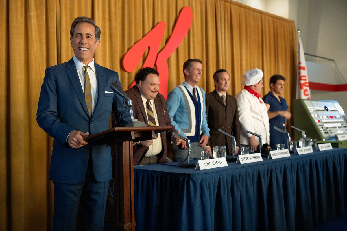 Seinfeld se tient derrière un podium devant le Kellogg's K aux côtés d'un panel d'autres personnes dans le film Netflix Unfrosted.