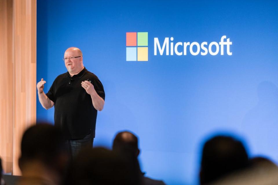 Kevin Scott, directeur technique de Microsoft, se présente sur scène devant un mur bleu portant le logo Microsoft.  Le public flou se dirige au premier plan.