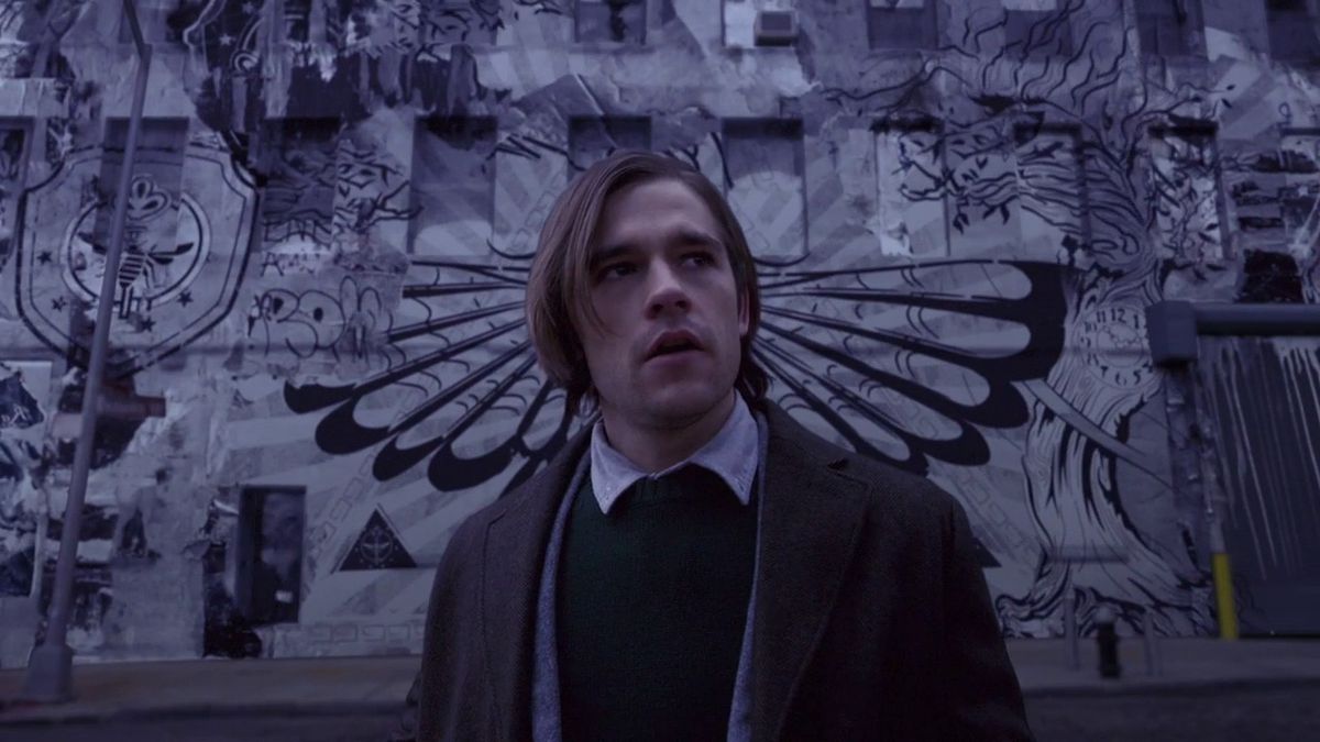 Quentin Coldwater se tient devant un mur couvert de graffitis dans une scène de The Magicians.