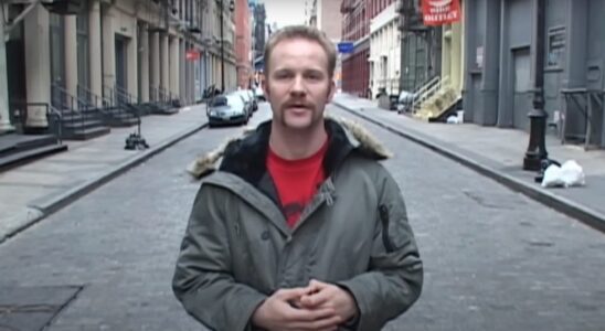 Morgan Spurlock speaking in the middle of the street, wearing a grey coat in Super Size Me.