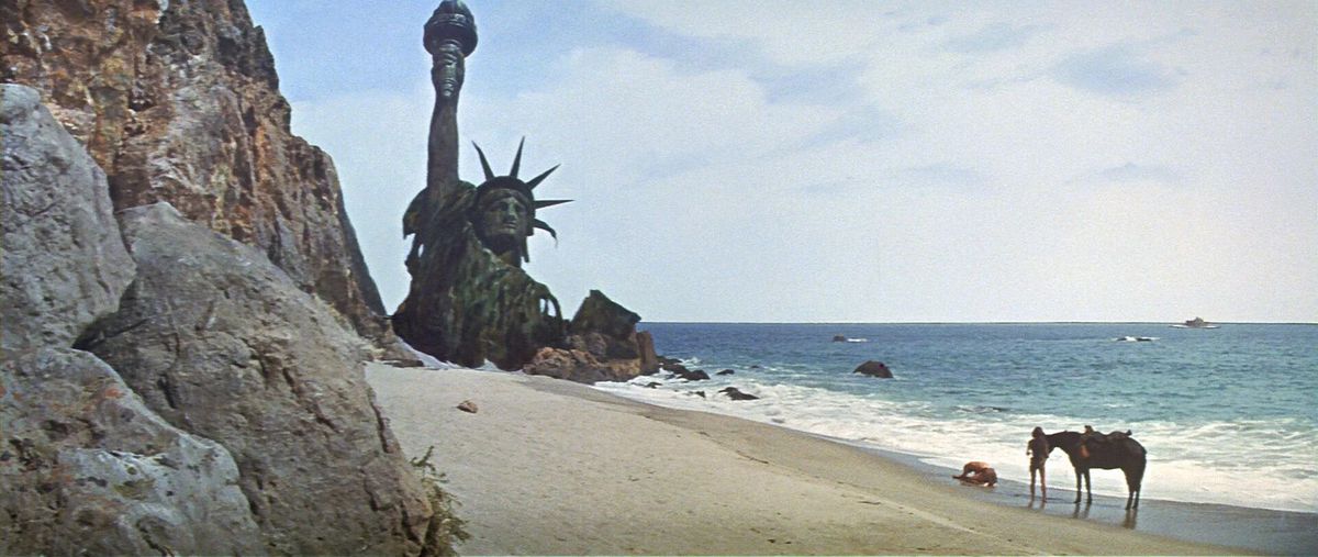Un homme affalé sur le bord de la plage avec une femme et un cheval derrière lui et les ruines de la Statue de la Liberté en arrière-plan.