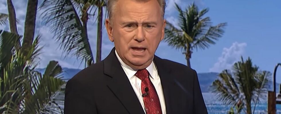 Pat Sajak in black suit and red tie hosting game of Wheel of Fortune