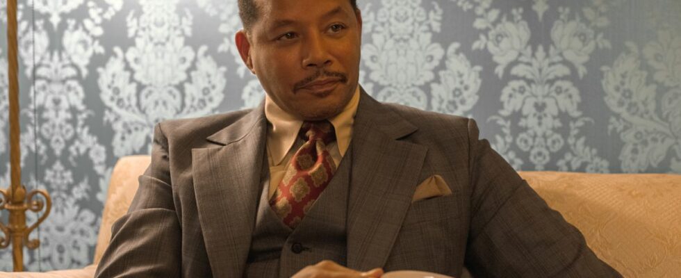 Terrence Howard sits on a couch, dressed in a suit and having a cup of coffee in Shirley.