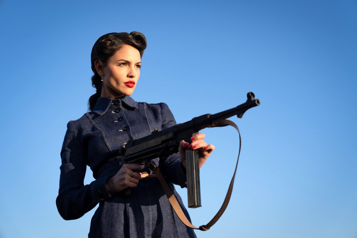 Eiza González, vêtue d'une robe élégante des années 1940 et d'un rouge à lèvres écarlate, tient une mitrailleuse dans le ministère de la Guerre anti-gentleman