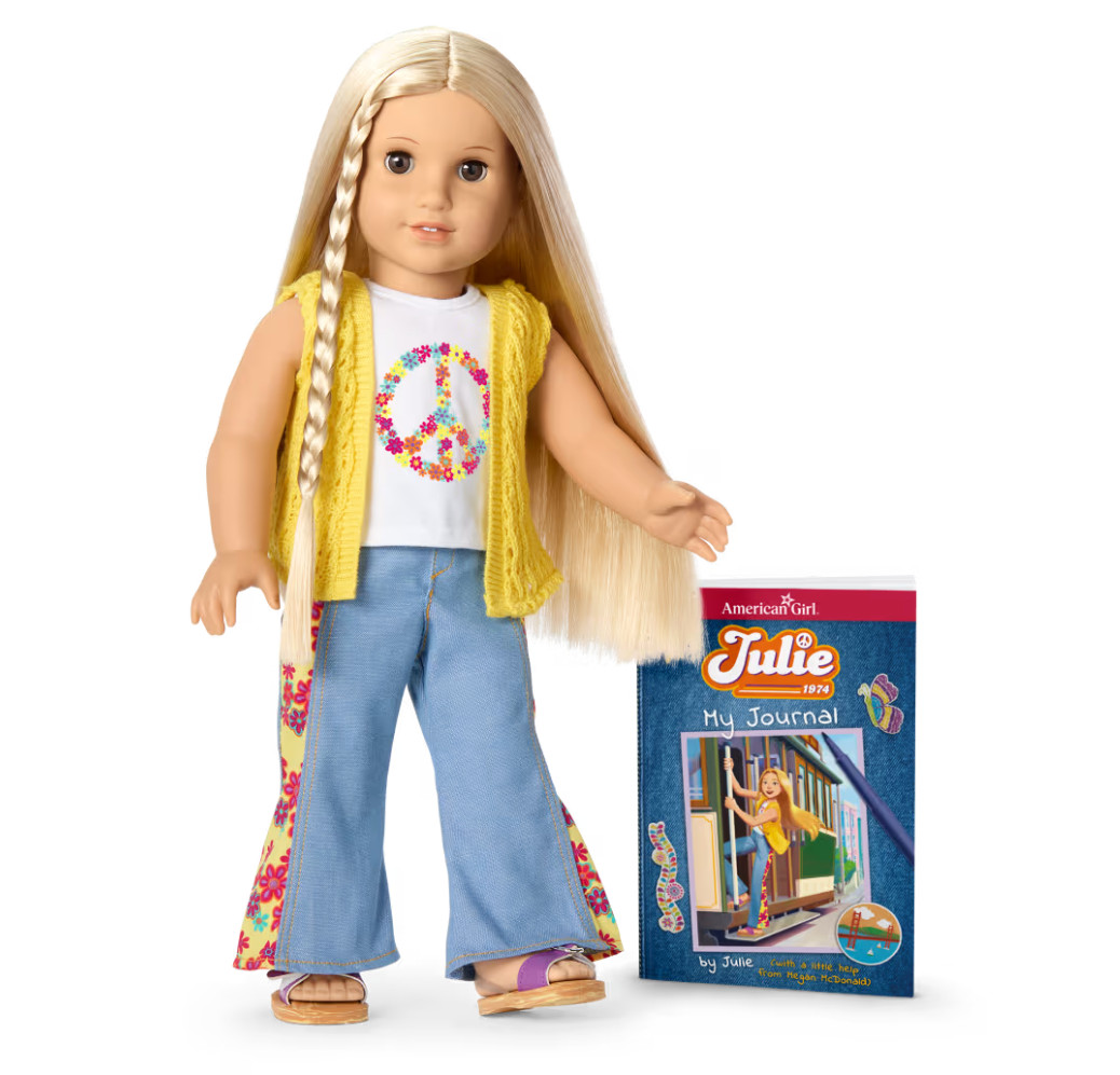 La poupée American Girl Julie est représentée portant sa tenue de personnage et debout à côté de son journal.