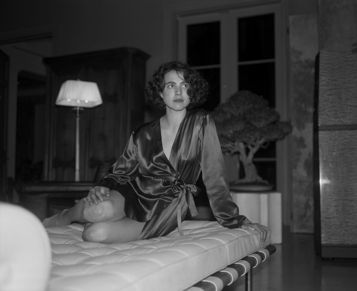 Margaret Qualley, photographiée en noir et blanc, est allongée sur un lit dans une robe de chambre en soie dans Kinds of Kindness