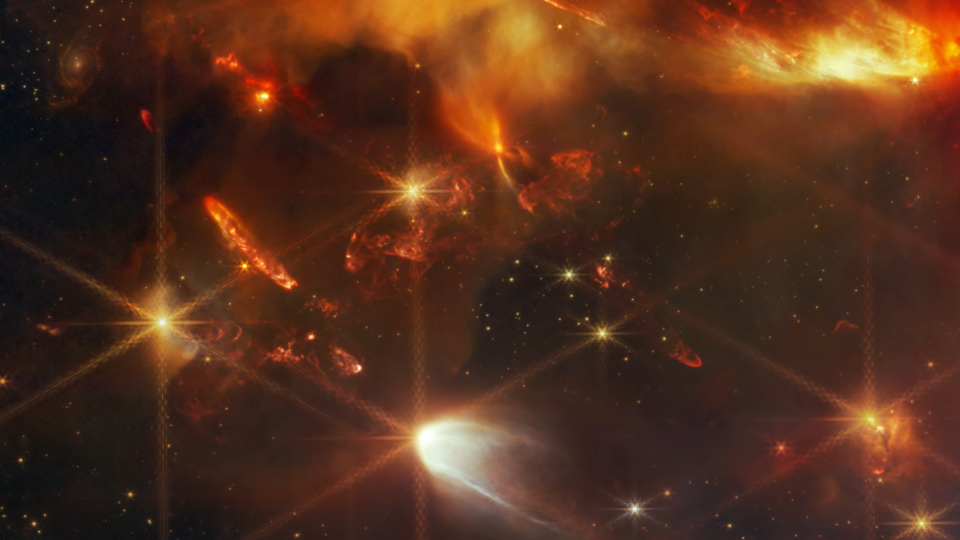 Jets perpendiculaires (considérés comme de minces faisceaux de lumière, semblables à des reflets de lentille) rayonnant à partir d'un amas d'étoiles rougeâtres.