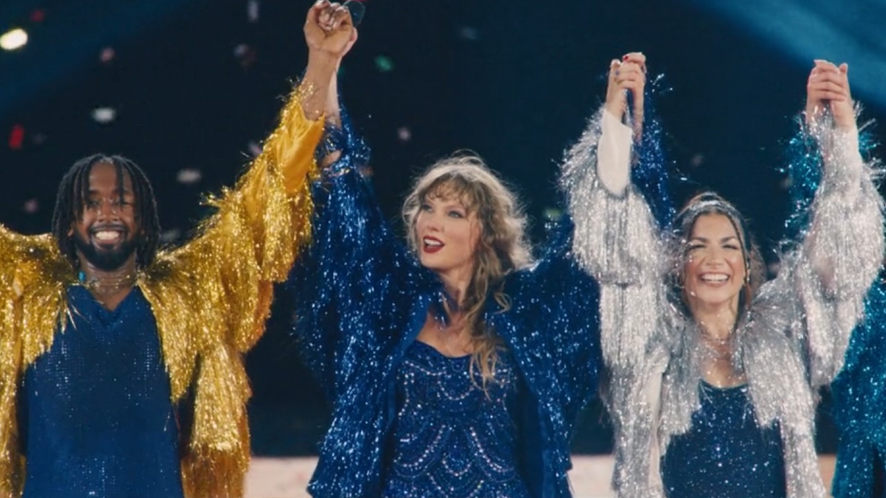 Taylor Swift tenant la main de deux de ses danseurs et levant leurs bras à la fin de la performance de Karma lors de la tournée Eras.