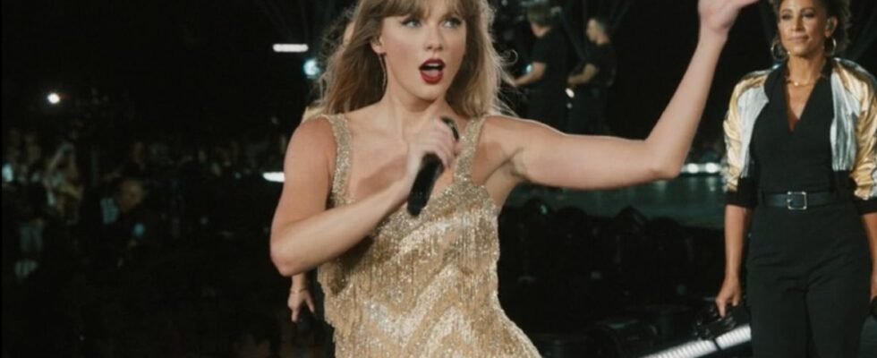 Taylor Swift holding her mic up and her free hand up while singing in the Fearless dress on The Eras Tour.