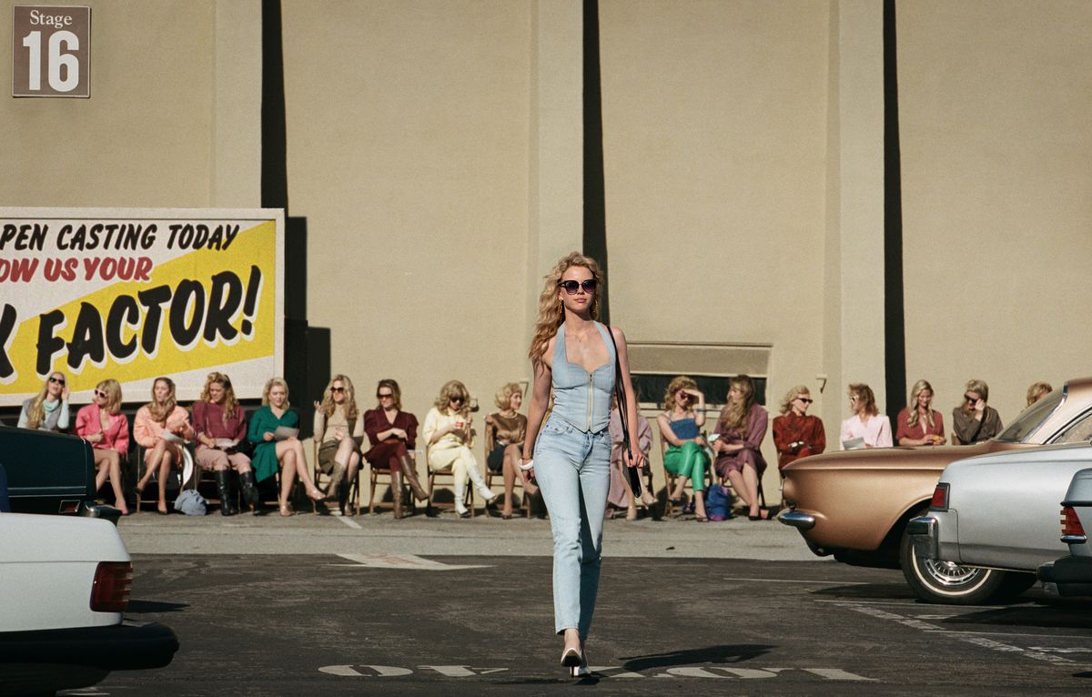 Maxine (Mia Goth) se pavane sur un parking d'Hollywood à l'extérieur d'un plateau de tournage de film, avec une rangée d'autres auditionneurs alignés sur des chaises derrière elle, en Maxxxine 