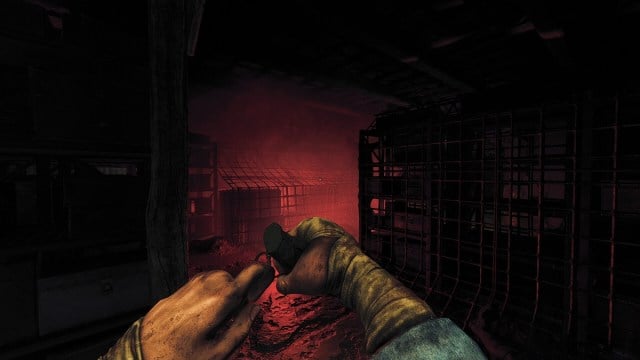 Amnesia The Bunker : le joueur retire la goupille d'une grenade tandis qu'une lueur rouge brille devant lui.