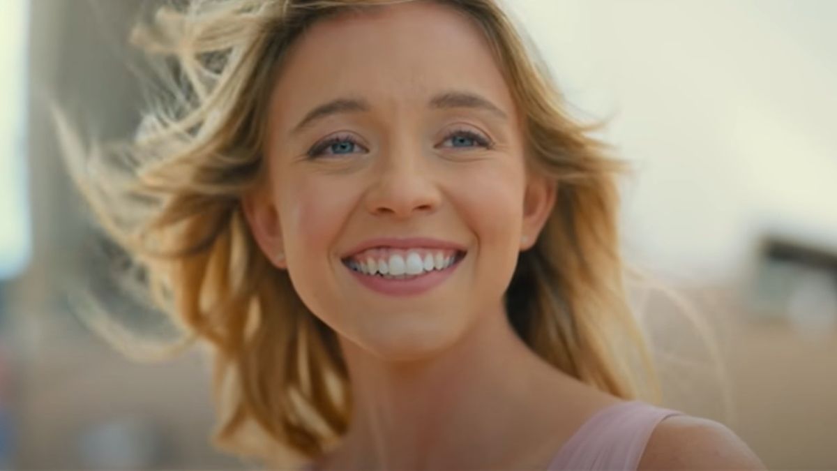 Sydney Sweeney smiling while they wind blows her hair away fromher face in Anyone But You.