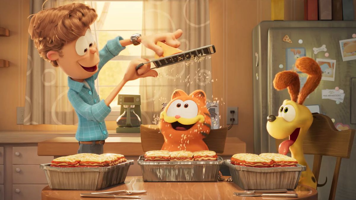 Jon Arbuckle râpe du parmesan sur les lasagnes de Garfield pendant qu'Odie regarde une image tirée du film Garfield