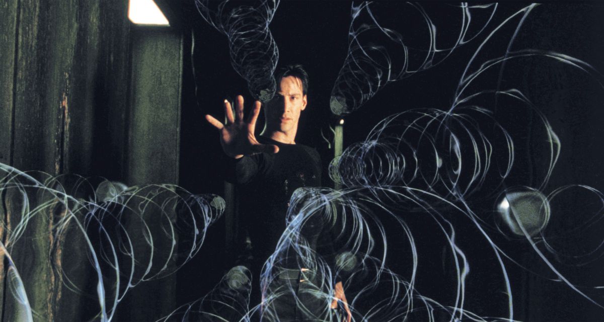 Un homme (Keanu Reeves) se tient dans un couloir, la main droite tendue, tandis qu'une grêle de balles suivies d'anneaux de mouvement visibles sont suspendues en mouvement devant lui.