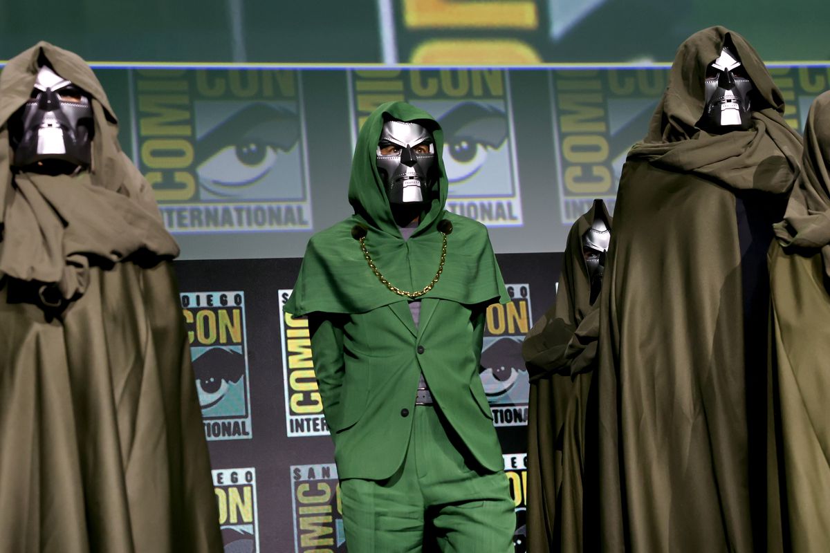 Robert Downey Jr. dans un costume vert à capuche avec une chaîne en or (très Doctor Doom) portant un masque Doctor Doom sur scène lors du panel Marvel Studios au SDCC 2024. 