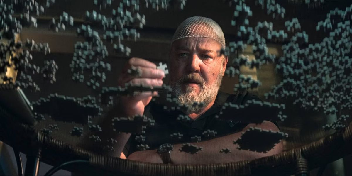 Un homme portant un filet à cheveux tenant une pièce de puzzle tout en regardant une table en verre remplie de pièces de puzzle.