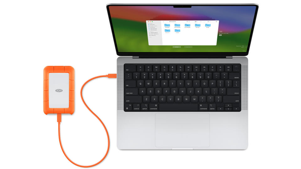 Vue aérienne d'un MacBook Pro ouvert avec un disque dur externe orange branché (à gauche).
