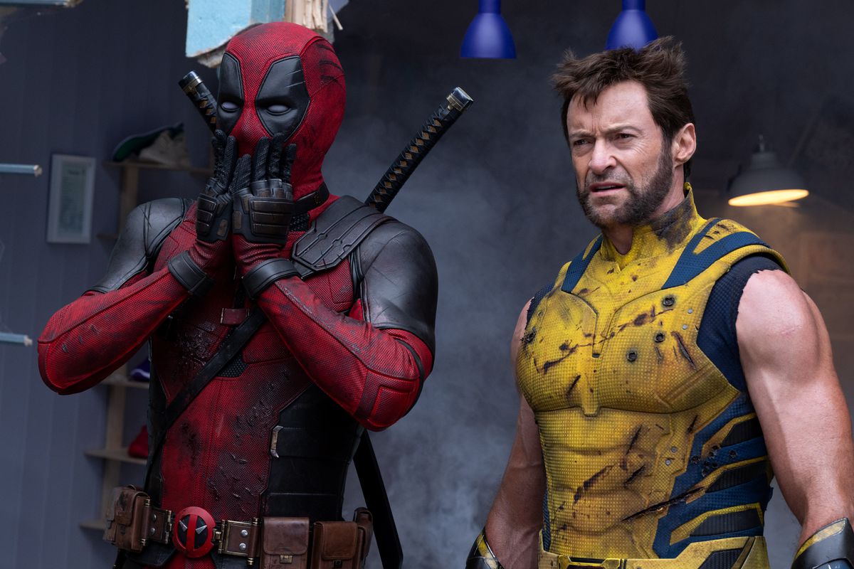 Un Deadpool marqué par la bataille met ses mains sur sa bouche en état de choc tandis qu'un Wolverine battu a l'air fatigué à côté de lui dans une scène du film Deadpool & Wolverine