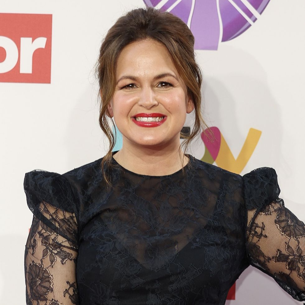 giovanna fletcher, une femme aux cheveux bruns relevés, portant du rouge à lèvres rouge et une robe noire, posant avec sa main sur sa hanche et souriant à la caméra sur le tapis rouge