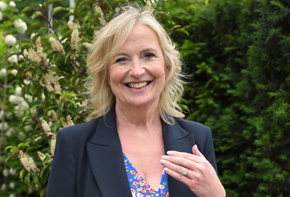 Carol Kirkwood sourit et lève la main pour montrer aux photographes sa bague de fiançailles alors qu'elle se tient devant une composition florale