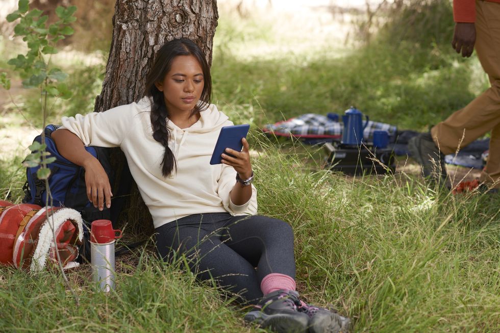 une femme assise dans un parc tenant un Kindle Paperwhite en denim