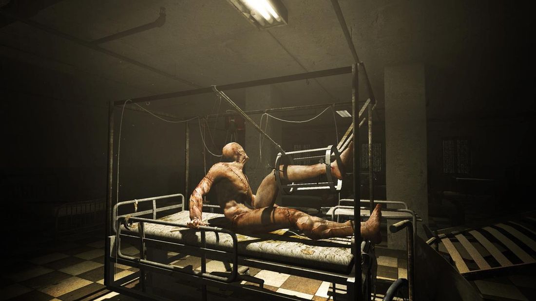 Une capture d'écran du jeu d'horreur Outlast représentant une personne nue attachée à un brancard, son corps couvert de cicatrices