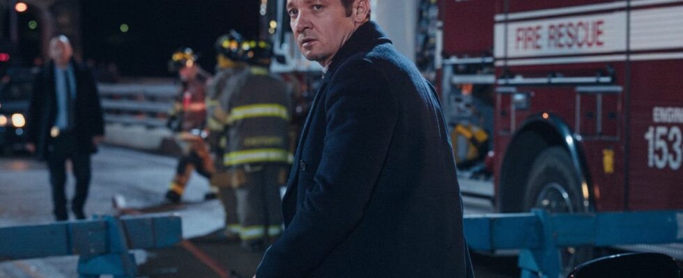 Jeremy Renner looking over his shoulder with a crime scene behind him in Mayor of Kingstown.