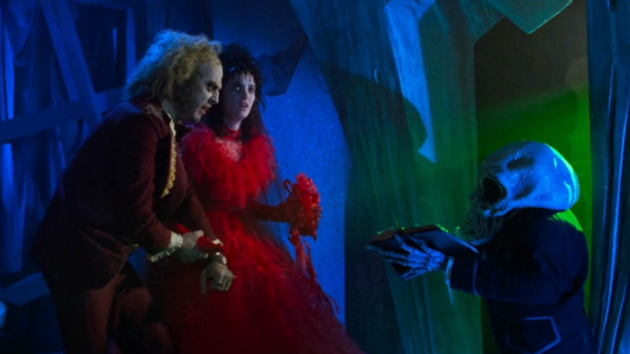 Michael Keaton dans le rôle de Beetlejuice et Winona Ryder dans une grande robe rouge dans le rôle de Lydia parlant à un petit extraterrestre dans Beetlejuice.