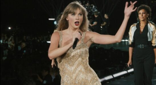 Taylor Swift holding her mic up and her free hand up while singing in the Fearless dress on The Eras Tour.