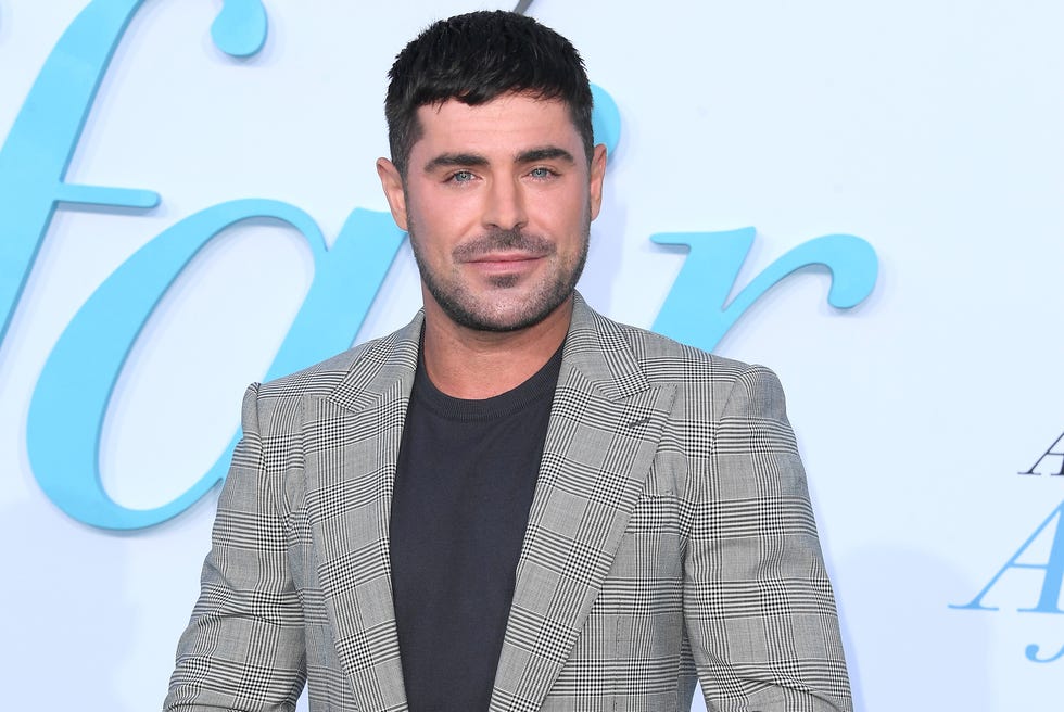 Zac Efron porte un costume gris et un t-shirt noir alors qu'il pose pour une photo